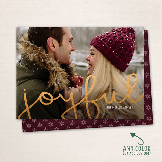 Couple smiling at each other in the snow with “Joyful” written in gold script across the photo, customizable color options shown with a matching snowflake patterned back.