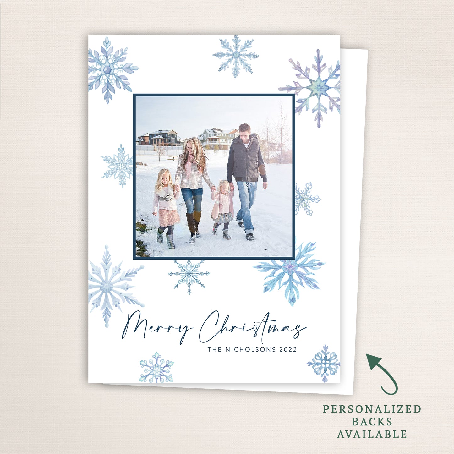 “Merry Christmas” snowflake photo card from Halo Design Shop featuring a centered family photo framed in navy blue, surrounded by watercolor snowflakes in cool winter tones. Includes customizable text, color options, and optional personalized backs.