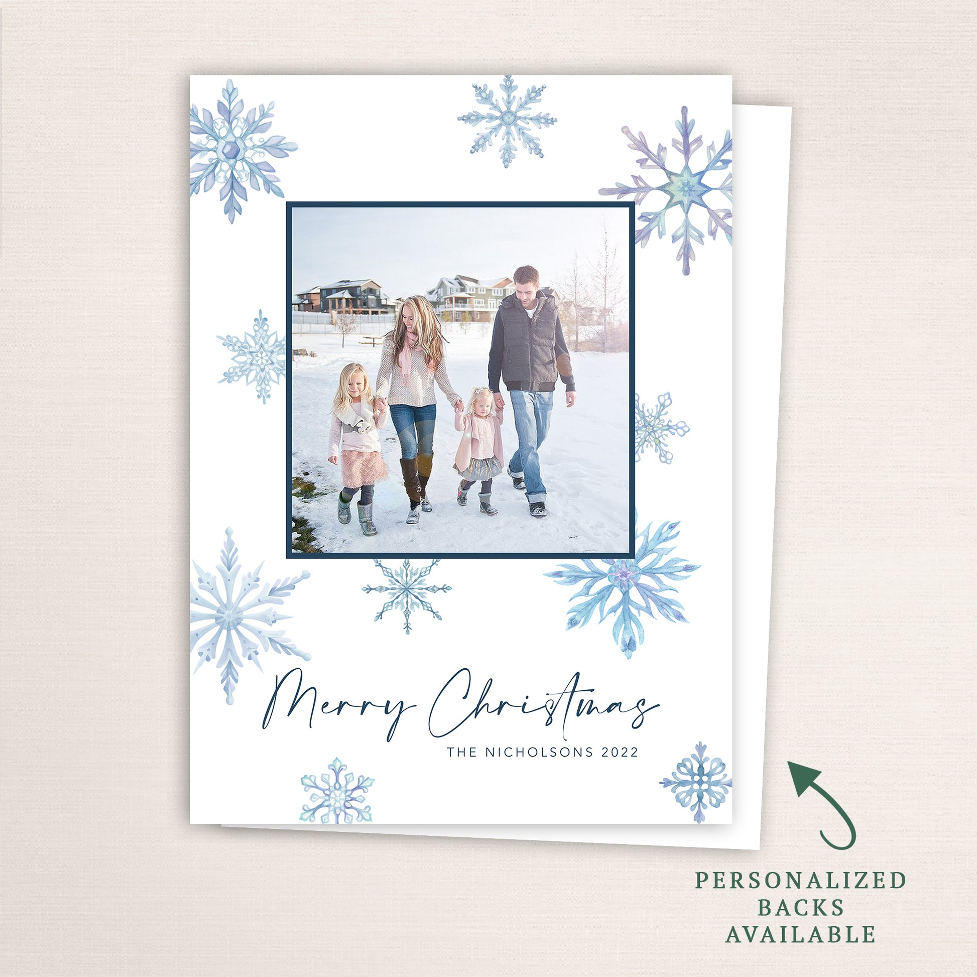 “Merry Christmas” snowflake photo card from Halo Design Shop featuring a centered family photo framed in navy blue, surrounded by watercolor snowflakes in cool winter tones. Includes customizable text, color options, and optional personalized backs.