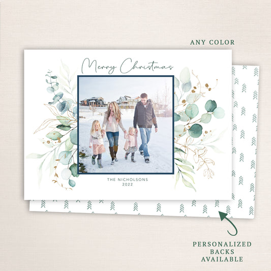 “Merry Christmas” eucalyptus photo card from Halo Design Shop featuring a modern botanical frame of soft green leaves and gold detailing, centered family photo, and customizable text. Includes personalized back options and any-color customization. White background option.