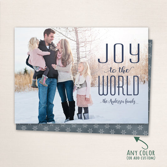 Family of four standing in the snow, smiling together under winter sunlight with the text “Joy to the World” and family name printed in elegant lettering on the right.