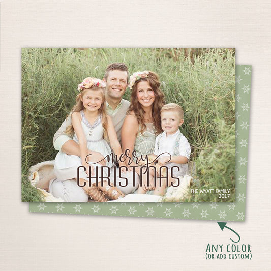 Horizontal holiday photo card featuring a family of four sitting outdoors among green foliage. The design includes “Merry Christmas” in elegant script with customizable colors and a matching snowflake-patterned back.
