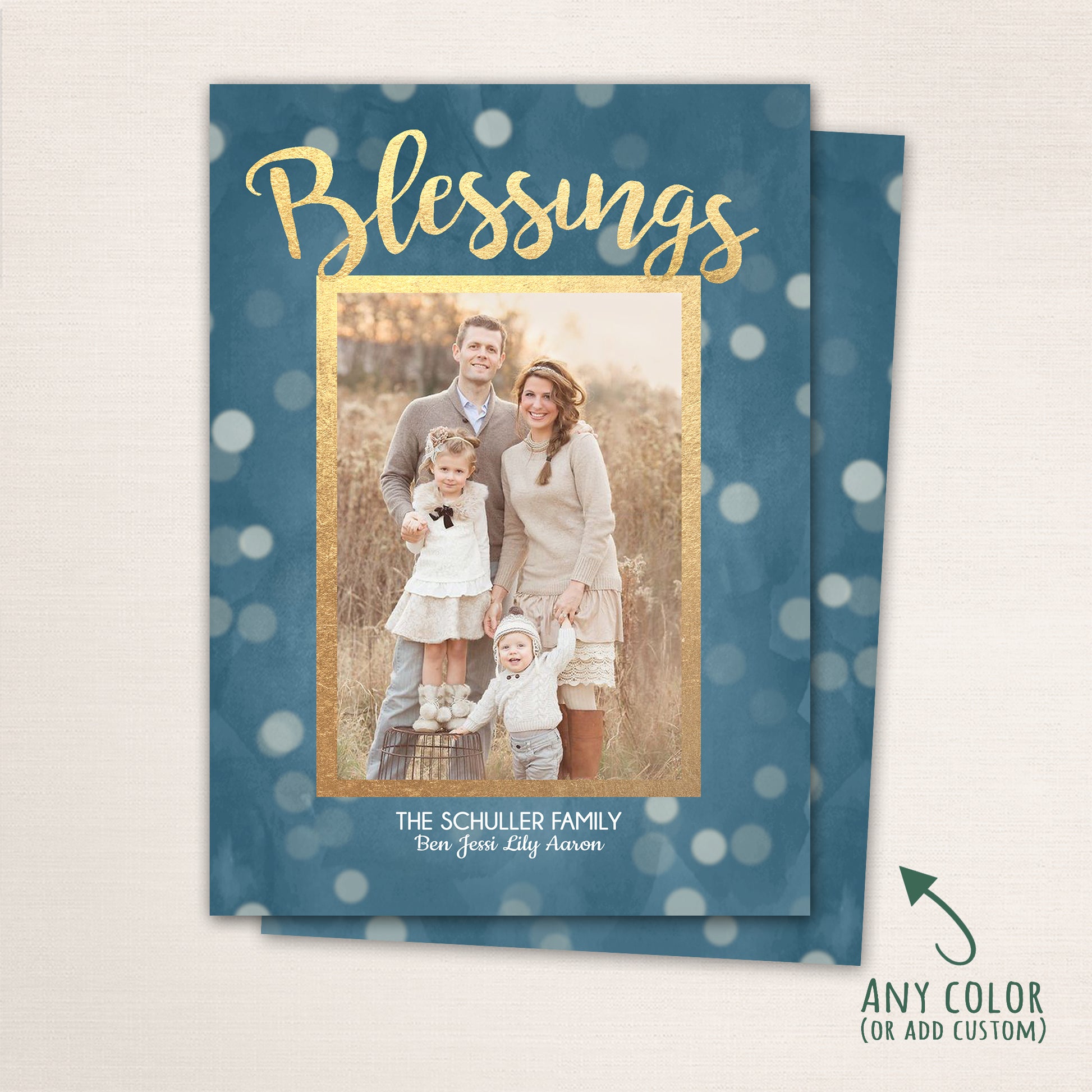 Vertical holiday card design featuring a family of four posing in a golden field, framed by a blue bokeh background and gold border. The word “Blessings” appears in metallic-style script at the top, with family names printed neatly below.