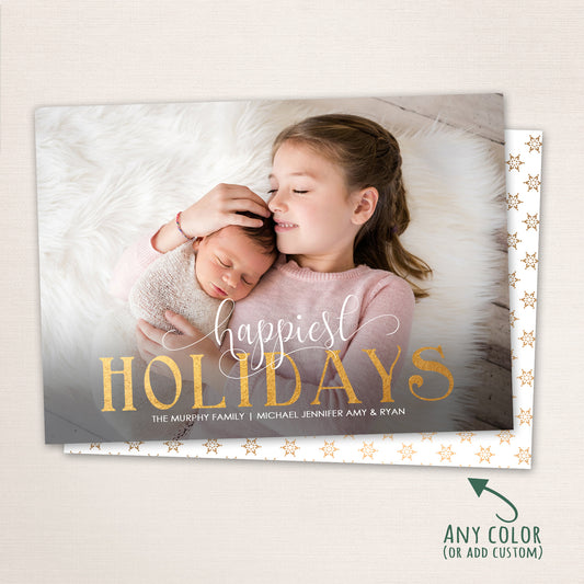 Sibling holiday card featuring newborn and older sister on white fur blanket with “Happiest Holidays” in gold with a snowflake patterned background.