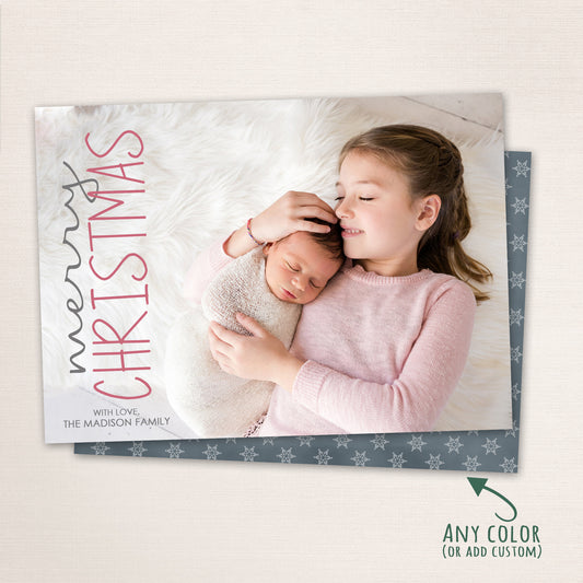 Sister lovingly holding her newborn sibling on a soft white blanket, with “Merry Christmas” written in elegant vertical lettering and family name printed below.