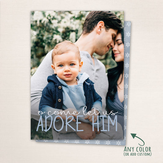 Vertical photo card featuring “O Come Let Us Adore Him” in soft blue script across a family portrait. The background includes subtle snowflake details, with the option to customize the color scheme for a personalized holiday design.