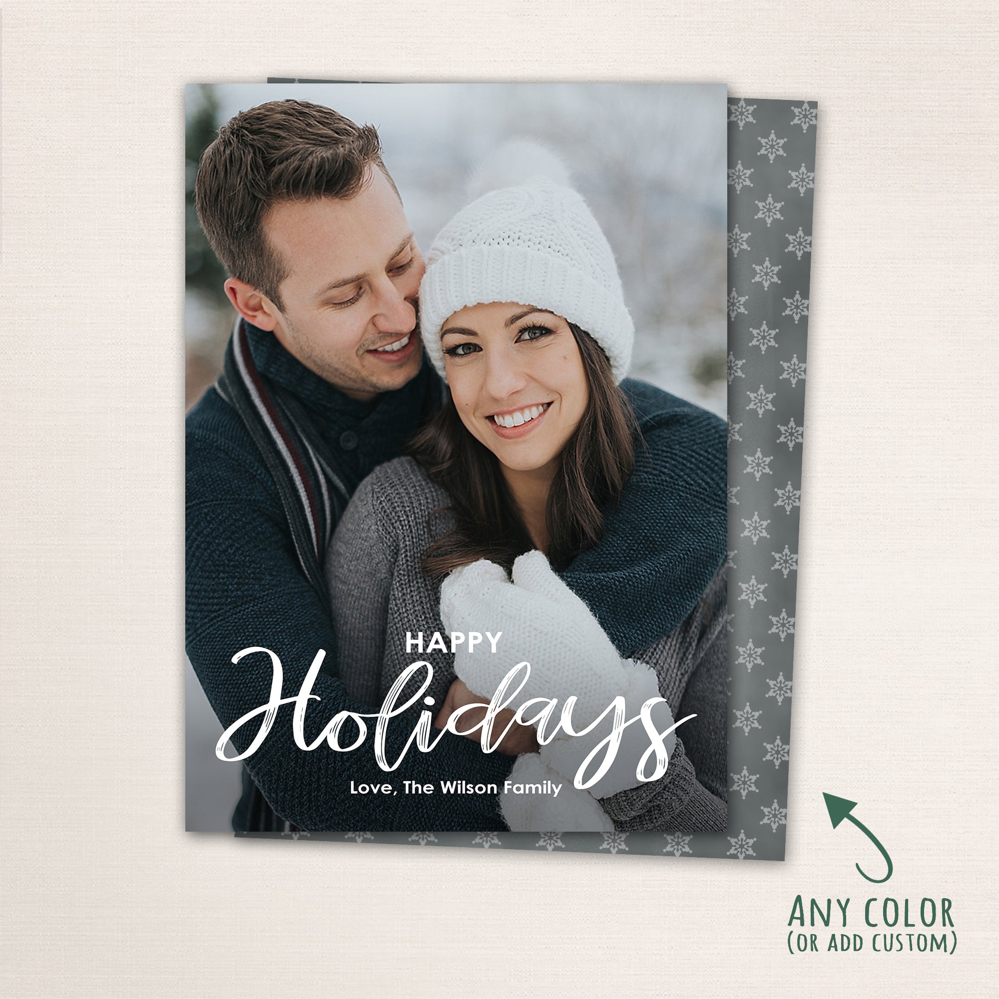 Snowy winter holiday photo card featuring a couple in cozy winter attire with “Happy Holidays” script, personalized text and a snowflake patterned back.