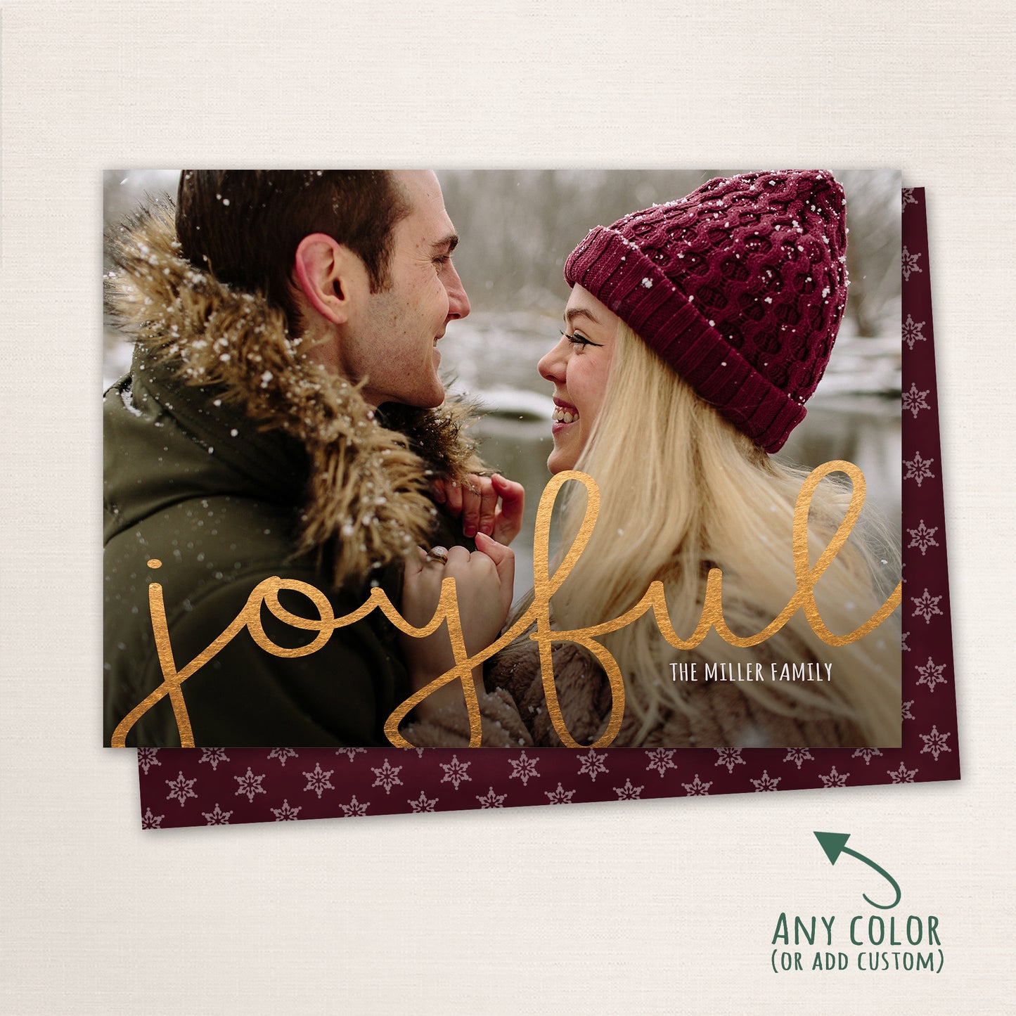 Couple smiling at each other in the snow with “Joyful” written in gold script across the photo, customizable color options shown with a matching snowflake patterned back.