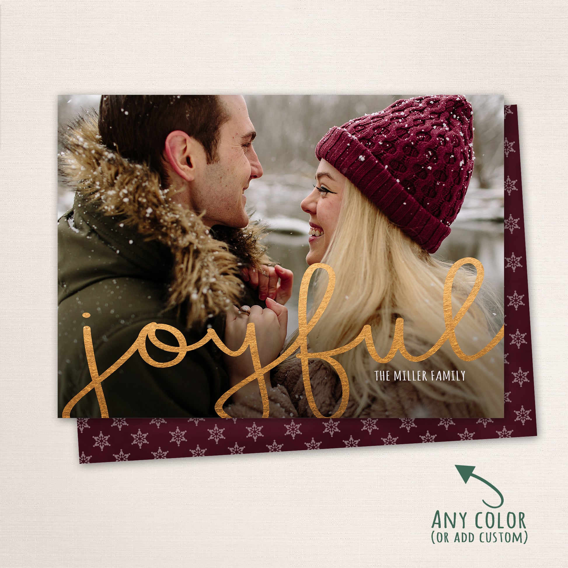 Couple smiling at each other in the snow with “Joyful” written in gold script across the photo, customizable color options shown with a matching snowflake patterned back.
