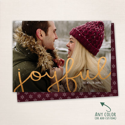 Couple smiling at each other in the snow with “Joyful” written in gold script across the photo, customizable color options shown with a matching snowflake patterned back.