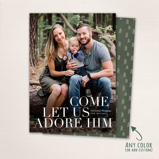 Christian Christmas photo card featuring a family sitting outdoors with large white text reading “Come Let Us Adore Him,” customizable with family name and holiday message.