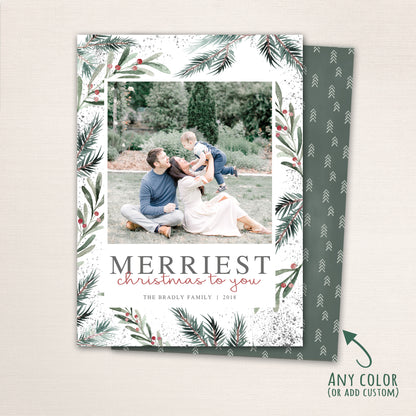 Merriest Christmas botanical photo card with watercolor pine branches and berries surrounding a family photo, featuring customizable names and year in modern typography.