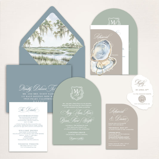 Dusty blue and sage Charleston wedding invitation suite with custom watercolor marsh envelope liner, oyster shell artwork, arched monogram invitation, rehearsal dinner card, details card, and deckle edge QR code RSVP for an elegant Lowcountry wedding.