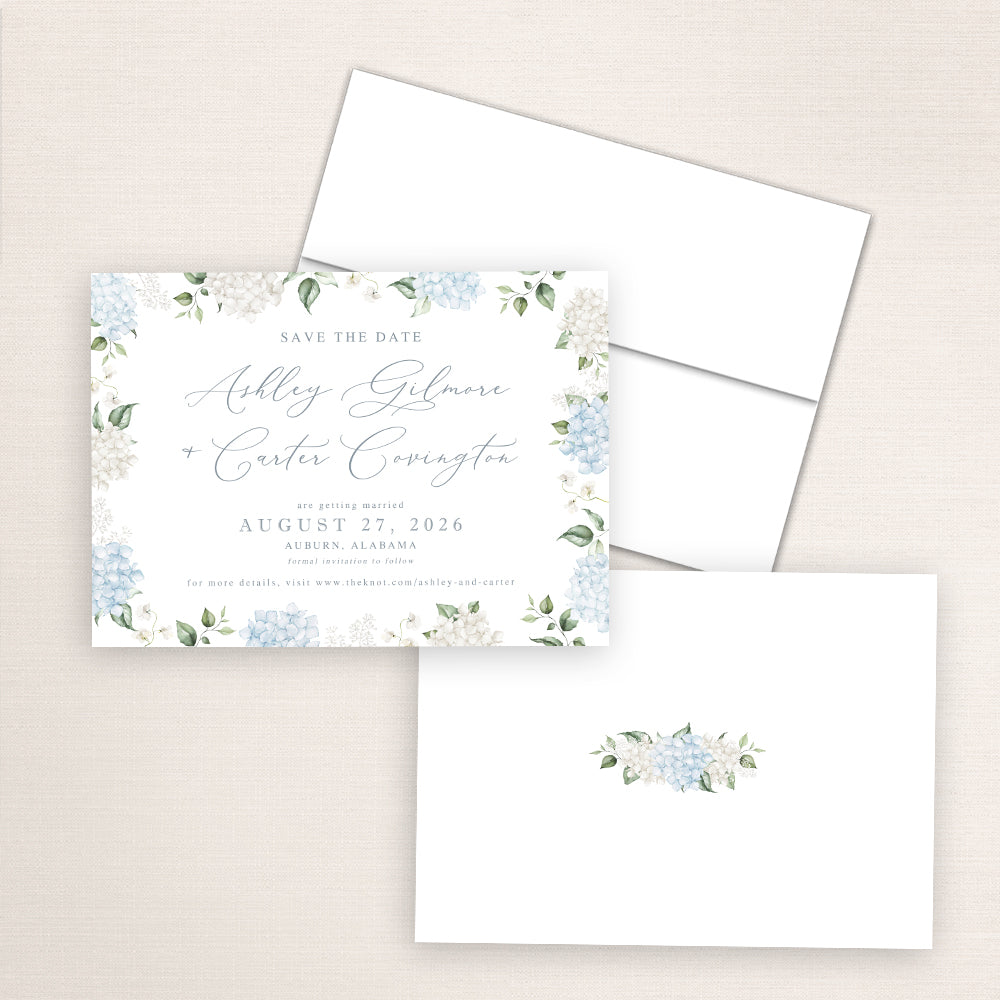 Floral save the date card surrounded by watercolor blue and white hydrangeas with elegant script fonts displaying the couple’s names, Ashley Gilmore and Carter Covington, and wedding details for August 27, 2026, in Auburn, Alabama.