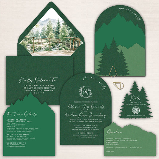 Dark forest green mountain wedding invitations featuring layered laser cut mountain silhouettes, evergreen pine trees, arched invitation cards, watercolor mountain venue envelope liner, coordinating details and reception cards, and a pine tree QR code RSVP. Nature inspired wedding stationery for an elegant mountain or woodland celebration.