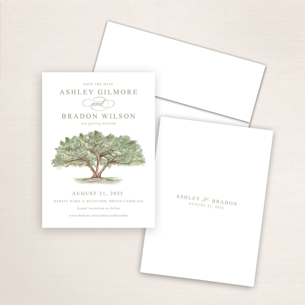 Vertical save the date card featuring a hand-painted watercolor an oak tree with lush green leaves. The design includes elegant serif and script fonts announcing a wedding date with the couples names and date also printed on the back and an included white envelope.