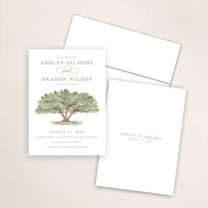Vertical save the date card featuring a hand-painted watercolor an oak tree with lush green leaves. The design includes elegant serif and script fonts announcing a wedding date with the couples names and date also printed on the back and an included white envelope.
