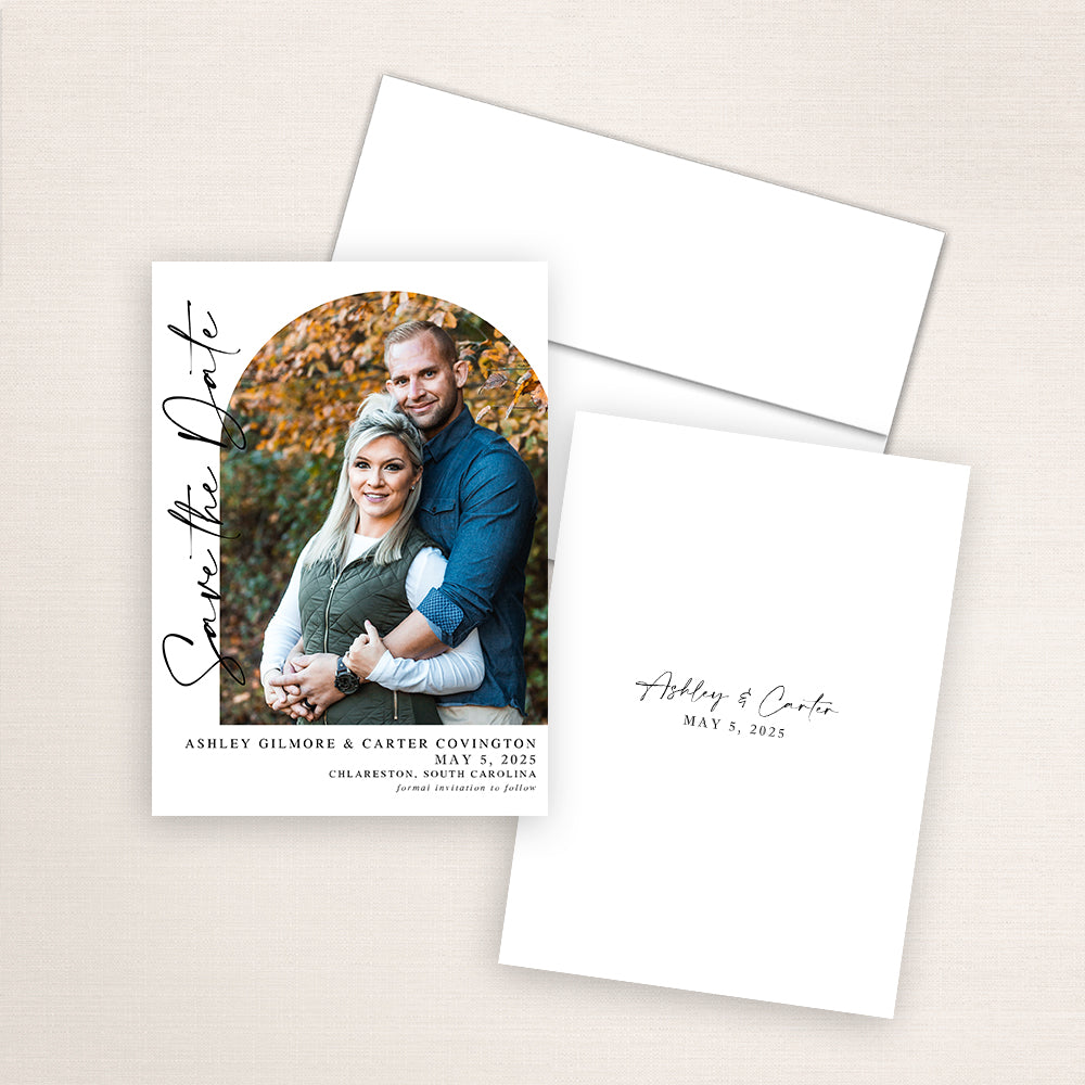 Modern photo save the date card featuring a vertical layout with an arched photo of a couple surrounded by autumn leaves. Elegant black script reads “Save the Date” along the side, with wedding details printed below. The matching back design includes their names and wedding date in minimalist black script.