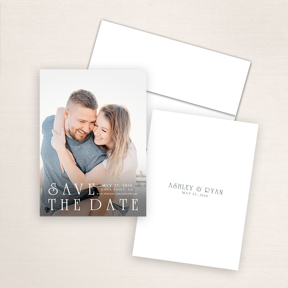 Minimalist photo save the date card featuring a photo of the couple embracing at the beach with soft natural light. The design showcases elegant serif text reading “Save the Date” with wedding date, location, and website.