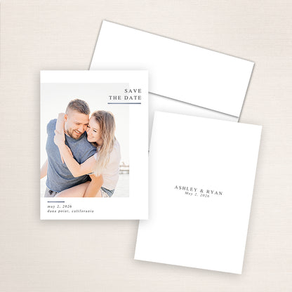 Modern minimalist photo save the date card featuring a couple embracing at the beach with natural sunlight. The design includes classic serif text reading “Save the Date” in the upper right corner with wedding details for Ashley and Ryan below.