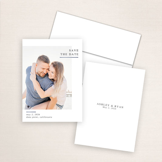 Modern minimalist photo save the date card featuring a couple embracing at the beach with natural sunlight. The design includes classic serif text reading “Save the Date” in the upper right corner with wedding details for Ashley and Ryan below.